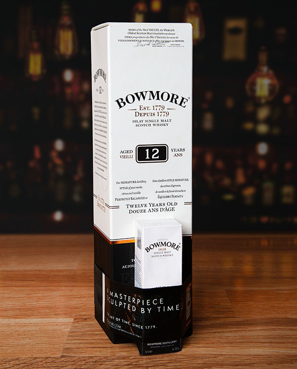 Bowmore 12 Year Old Islay Single Malt Scotch Whisky box with a smaller box attached with elastomer band. Bottles partially visible behind.