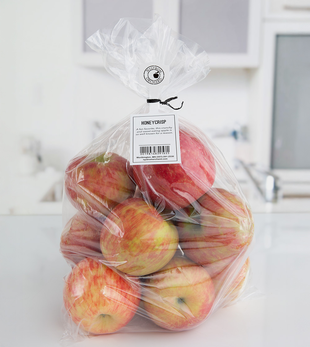 Bag of Honeycrisp apples from Nystrom Orchard with description, barcode, and contact info shared on a tag hanging from the bag opening by a black twist tie.