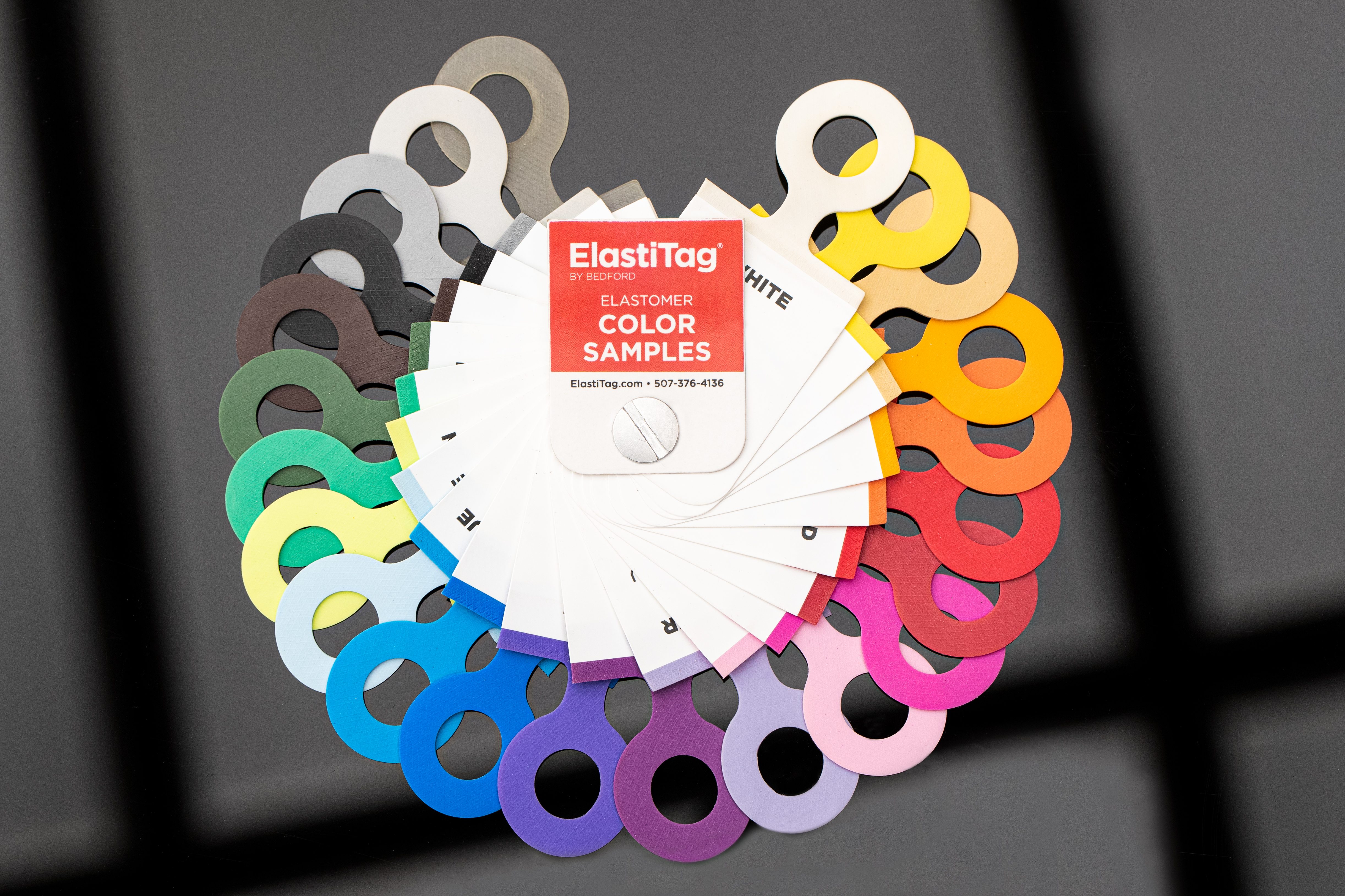 ElastiTag color samples fanned out. Red tag in center, various colored swatches with ring cutouts.