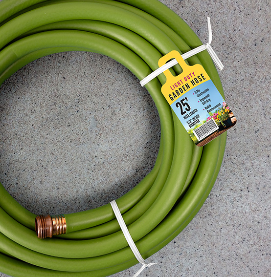A tag advertising a 25' garden hose attached to a white twist tie securing a green garden hose.