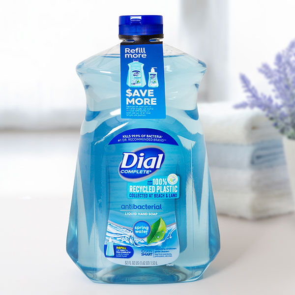 Dial Complete antibacterial hand soap bottle with "100% Recycled Plastic" label and "Save More" tag. Blue liquid, white background.