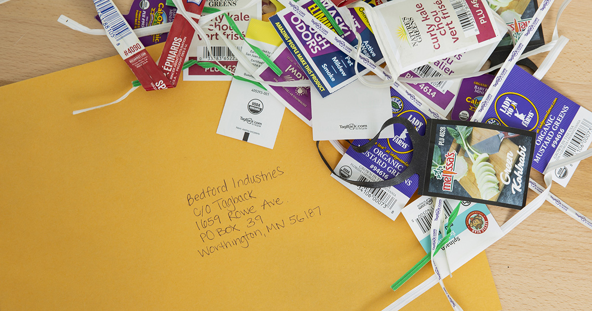 A yellow envelope with a handwritten address, surrounded by a pile of colorful twist ties and produce labels. The envelope is addressed to Bedford Industries in Worthington, MN.