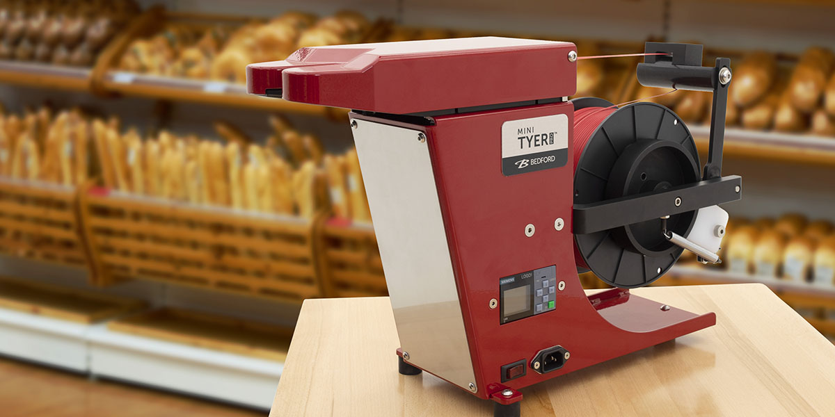 Red Mini Tyer Pro tie machine with baked goods in the background.