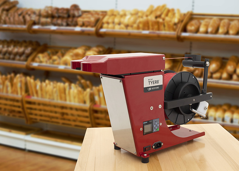Red Mini Tyer Pro twist tying machine with baked goods in the background.