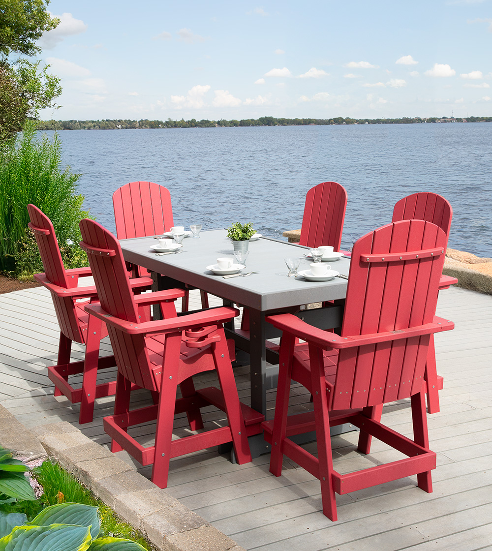 Red outdoor dining set with made of recycled plastic lumber with a gray tabletop and six chairs on a wooden deck near a body of water.