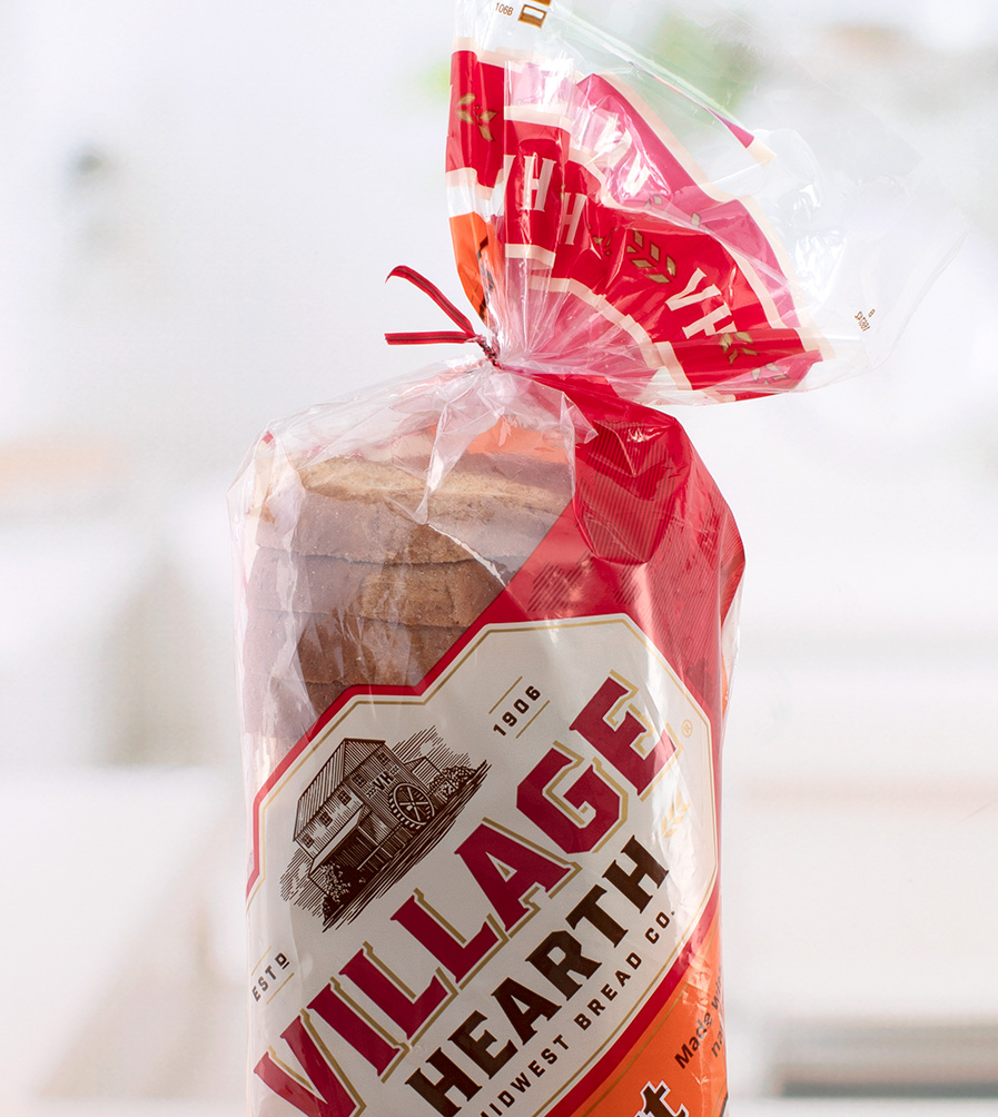 A red bread tie closes a bag of Village Hearth brand honey wheat bread.