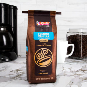 Brown Dunkin' Donuts French Vanilla coffee bag with black coffee tie on light marble counter with coffee pot in background.