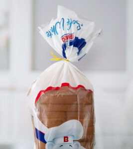 A loaf of white bread closed by a yellow twist tie with a light kitchen background.