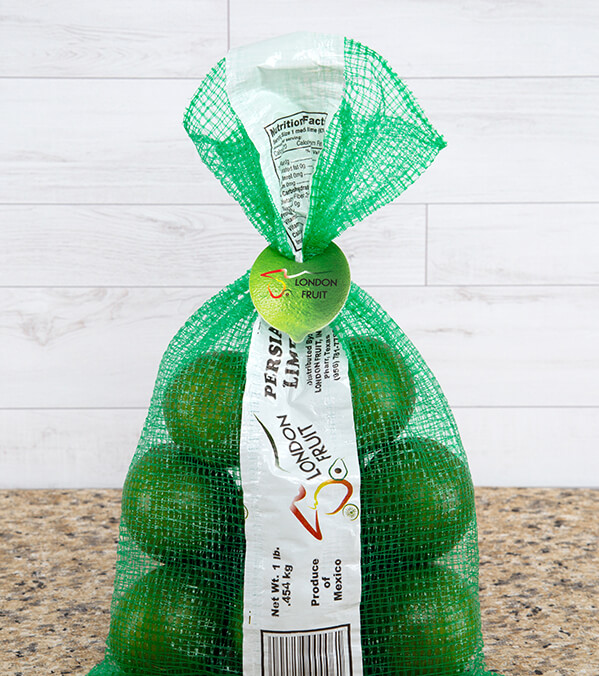 green mesh bag of limes on brown granite countertop closed by lime-shaped green clip tag with London Fruit brand.
