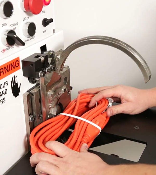 Bedford ring tier machine applying twist tie to orange extension cord.