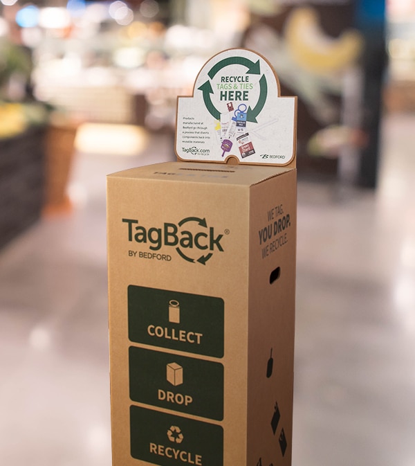 A tall cardboard box with small deposit hole, TagBack logo, and instructions: “Recycle Tags & Ties Here”