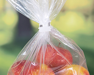 A compostable bag closure clip around a bag of red apples