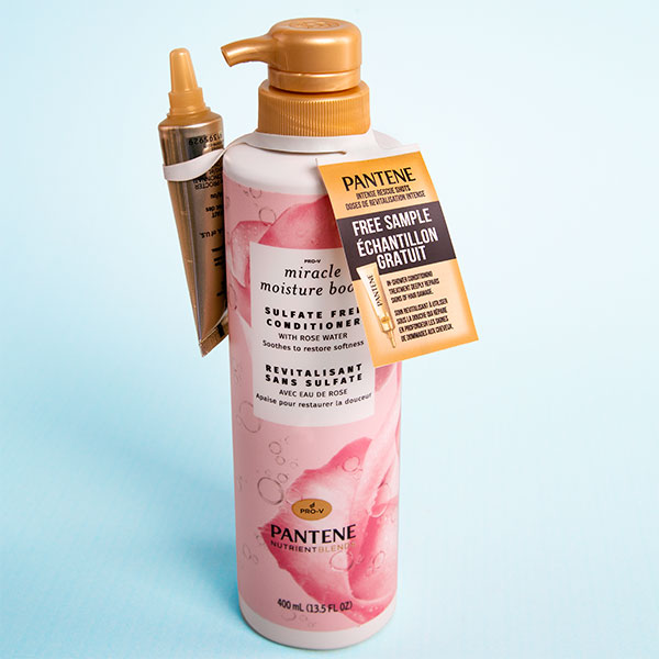 A bottle of Pantene Conditioner with a free sample bottle attached with a tote. The bottle is pink and white and has a picture of a rose on it.