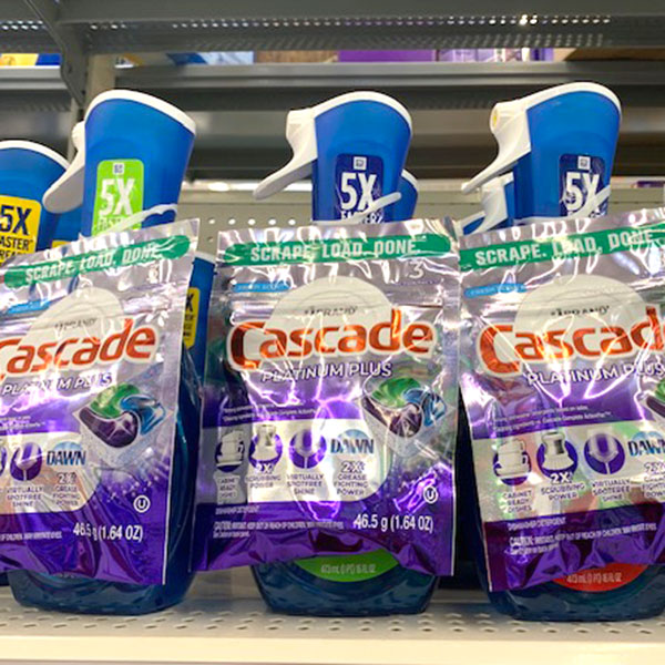 A photo of three sample pouches of Cascade Dish Detergent affixed to a bottle of Dawn dish with an ElastiTag tab on a store shelf.