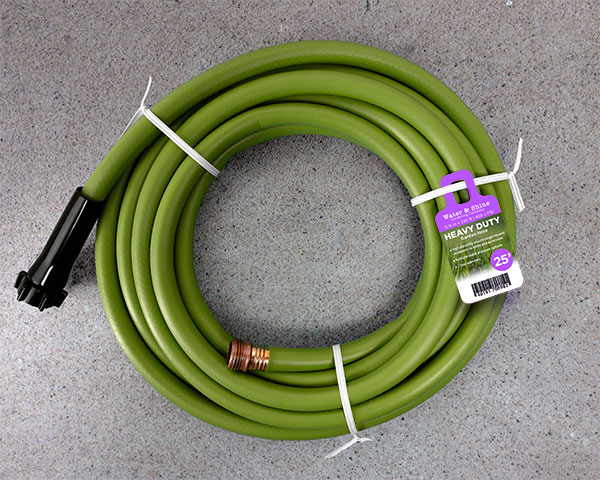 A green garden hose coiled up with twist tie and a Ring Tag attached noting the hose as "Heavy Duty" and 25 feet long.