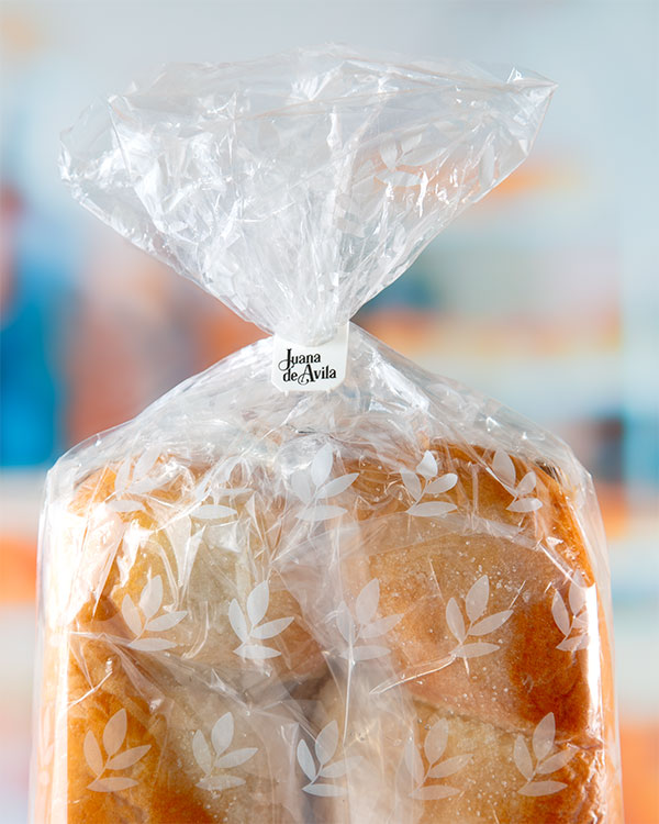 A close-up of a plastic bag of bread with a printed white bag closure label that says "Juana de Avila."